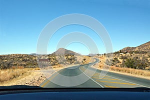Car view of a winding asphalt road in the desert in perspective with cars driving ahead under a blue sky