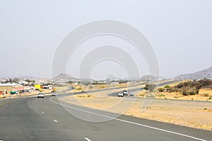 Car view of a winding asphalt road in the desert in perspective with cars driving ahead under a blue sky