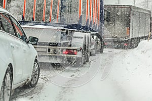 Car waiting behind large trucks during traffic jam on forest road, caused by heavy snow blizzard