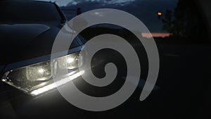 A car with the warning lights on stands on the side of the road at night. Traffic from cars with headlights on, car