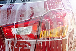 Car wash background. Close up of rear taillight on black modern luxury car covered with washing foam-soap