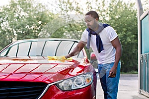 Car wash and cleaning at outdoors self service station. Shot of handsome bearded young African guy cleaning his red car