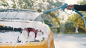 Car wash outdoors concept. Yellow car in foam. Car getting a wash with soap. Hand of African man with high pressure jet