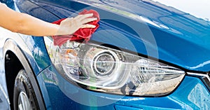 Car wash service. Man hand holding red microfiber cloth polish blue car and water drop after cleaning. Auto care service business