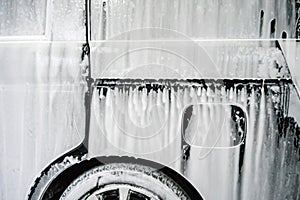 Car wash with soap. Black car covered by foam.