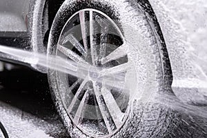 Car wash worker spraying car wheel and tire with white active cleaning foam