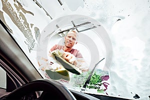 Car washing process: man washes front car window with soap