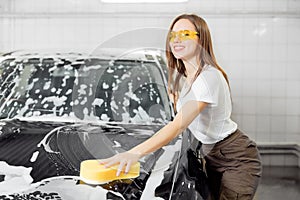 Car washing service. Worker beautiful woman cleaning auto black foam with yellow sponge
