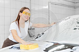 Car washing service. Worker beautiful woman cleaning auto black foam with yellow sponge