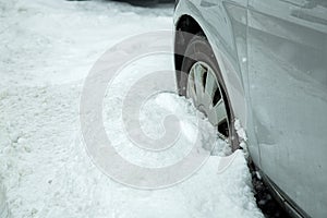 the car wheel of a gray vehicle is covered with snow, the car is blocked.