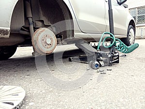 A car without a wheel, prepared for its replacement against the background of a Jack, side view - the concept of replacing