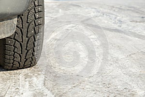 A car wheel on a slippery winter road. Close- up of studded rubber on ice. Dangerous driving conditions. Icy road with tracks from