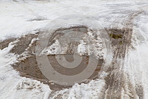 Car wheel and tire tracks on a small puddle of melted snow.