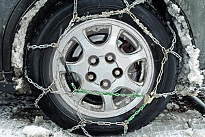 A car wheel wrapped with chains. Close-up. In the fenders of the car muddy snow. Snow chains on the car. Safety on