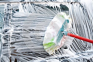 Car window covered with foam being wiped with a brush on the self service car wash