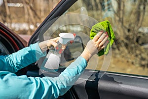 Car windows cleaning. female hands cleaning car window with green microfiber cloth and spray bottle with blank white label
