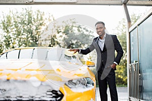 Car windscreen cleaning with yellow sponge and soap foam outdoors at car wash service