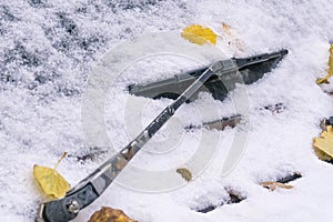 Car windshield covered with wet snow and yellow autumn leaves. Old rain wiper. Early winter