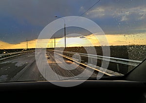 Car windshield with rain drops. View of the road across the bridge at sunset