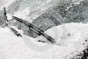 Car wiper blades clean snow from car windows. Flakes of snow covered the car with a thick layer. Safe driving