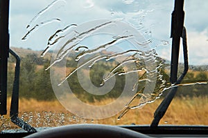 Car wiper cleaning rain drop on windshield. Driving in rain. Nature through window. Rainy weather and auto trip concept