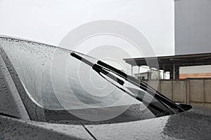 Car wipers cleaning water drops from windshield glass outdoors, closeup