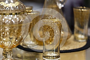 Carafe and several glass glasses on an ornate table in natural daylight.