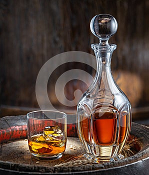 Carafe of whisky and glass of whisky on old wooden cask at the dark background