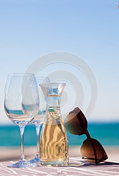 The carafe of white wine and a glass of wine with sunglasses by Garda Lake beach