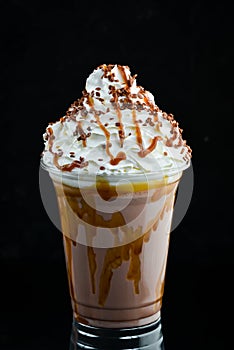 Caramel milkshake in a plastic cup. on a black background.