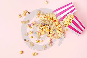 Caramel popcorn and dragee candies on pink background. Flat lay, top view.