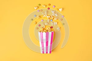 Caramel popcorn and dragee candies on yellow background. Flat lay, top view.