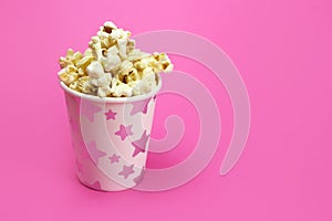 Caramel popcorn in a paper Cup on a pink background, copy space