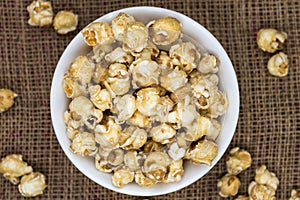 Caramel popcorn in white bowl on gunny sack.