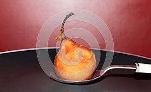 Caramelized pear, winter dessert, on metal spoon with white plastic handle, on black plate with white edge and red background