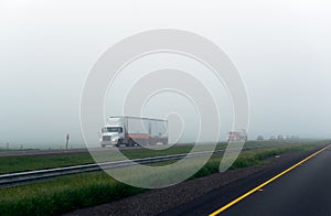 Caravan of big rigs semi trucks on the foggy highway