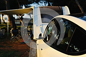 Caravan and electric car at sunset in caravan park. Camping in nature. Vacation and trip with mobile caravan home.