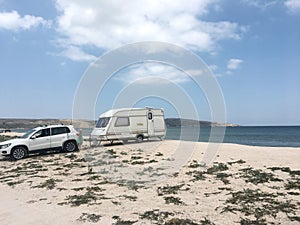 caravan trailer and car are parked on the beach near the very sea water. Summer holidays. Transport, RV, motorhome