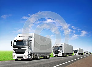 Caravan of white trucks on highway under blue sky