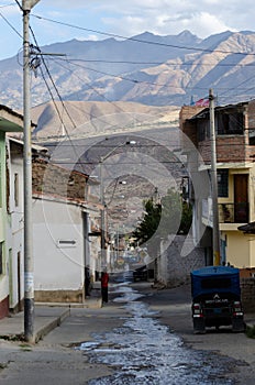 Caraz, Peru, July 19, 2010:  typical street of Peruvian town with motorcycle car and wet ground with mountains in the background