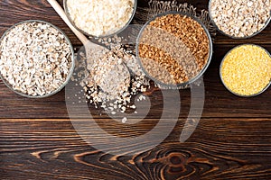 Carbohydrates. Various grain flakes in bowls on wooden. Oat, corn, rice, buckwheat, rye and wheat flakes.