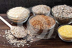 Carbohydrates. Various grain flakes in bowls on wooden. Oat, corn, rice, buckwheat, rye and wheat flakes.