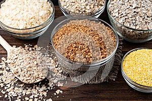 Carbohydrates. Various grain flakes in bowls on wooden. Oat, corn, rice, buckwheat, rye and wheat flakes.