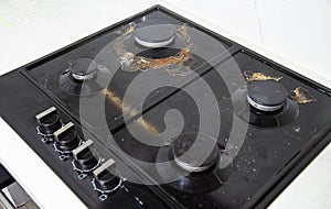 Carbon deposits and dirt on a black built-in gas stove. Cleaning kitchen appliances, close-up