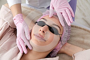 Carbon peeling in beauty salon. Cosmetologist applying black mask on the face of a beautiful woman for carbon peeling