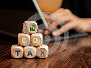 Carbon tax. Industrial factory icon on wood cube blocks stack with green text, CO2 TAX on desk with businessman with laptop.