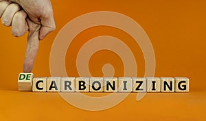 Carbonizing or decarbonizing symbol. Businessman turns wooden cube and changes words `carbonizing` to `decarbonizing`. Orange