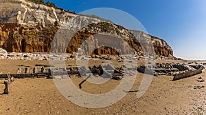 A carcass of a shipwreck on Old Hunstanton Beach resting beneath the white, red and orange stratified cliffs in UK