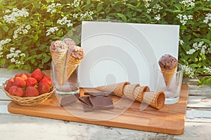 Card, chocolate ice cream, dark chocolate, basket of fresh strawberry and empty waffle cones near on rustic wooden table