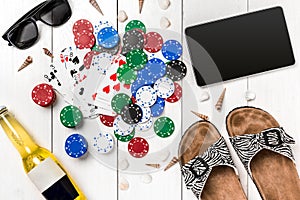 Card deck surrounded by poker chips and scattered seashells on white wooden background with copy space